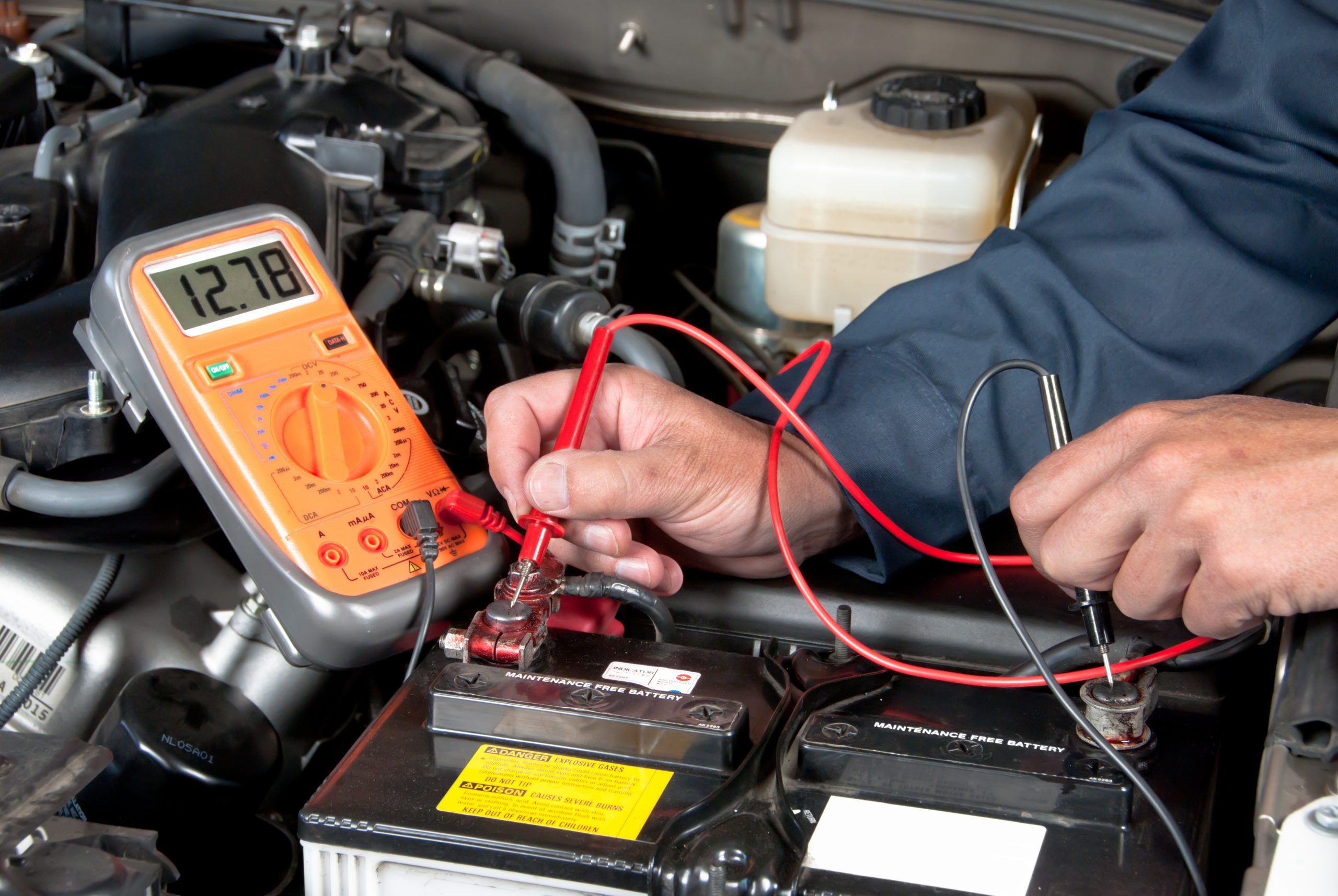 Check alternator repair. An auto mechanic uses a multimeter voltmeter to check the voltage level in a car battery.